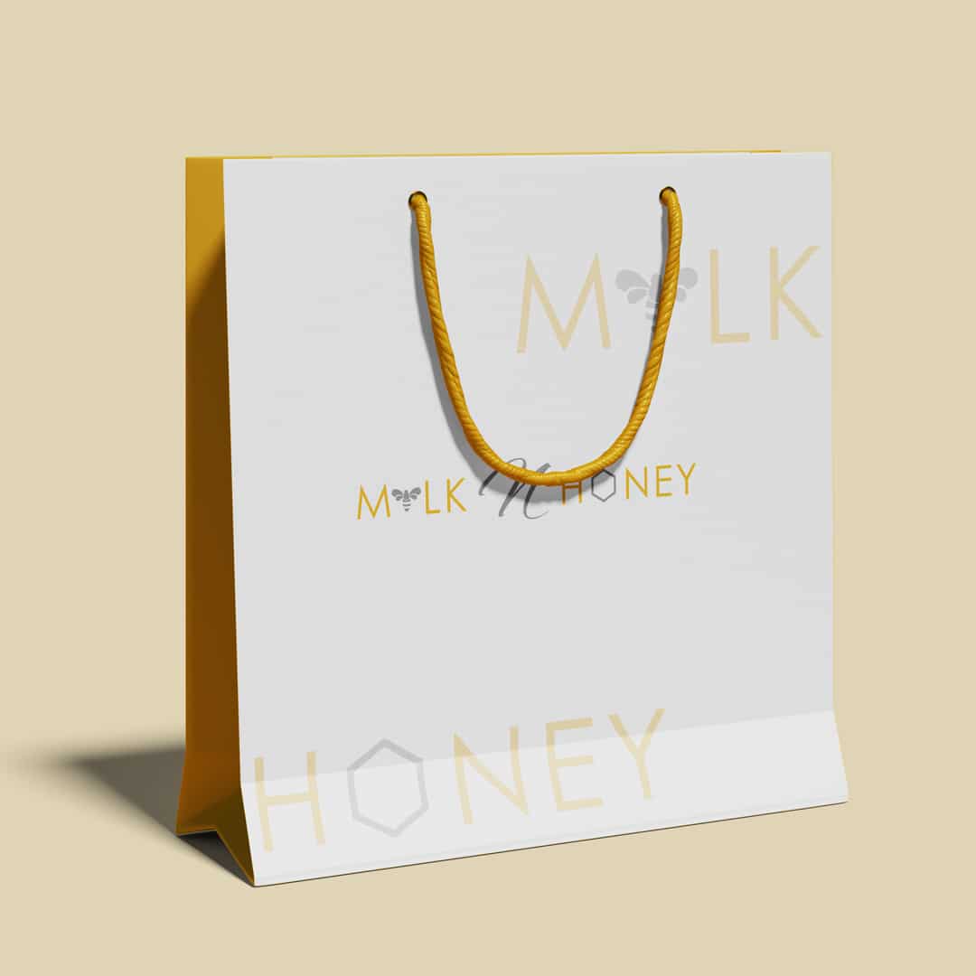 White shopping bag mockup with Milk n Honey branding in yellow and gray, featuring minimalist typography and bee motif