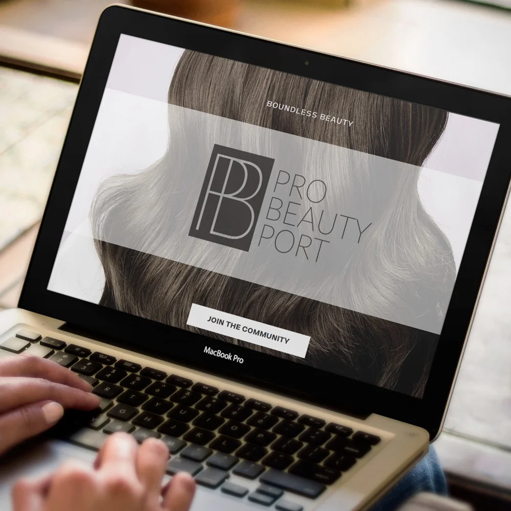Beauty Omaha Branding Omaha branding services website mockup displayed on a laptop screen, showing a beauty brand homepage with a close-up of flowing silver hair and a call-to-action button, photographed on a wooden desk.
