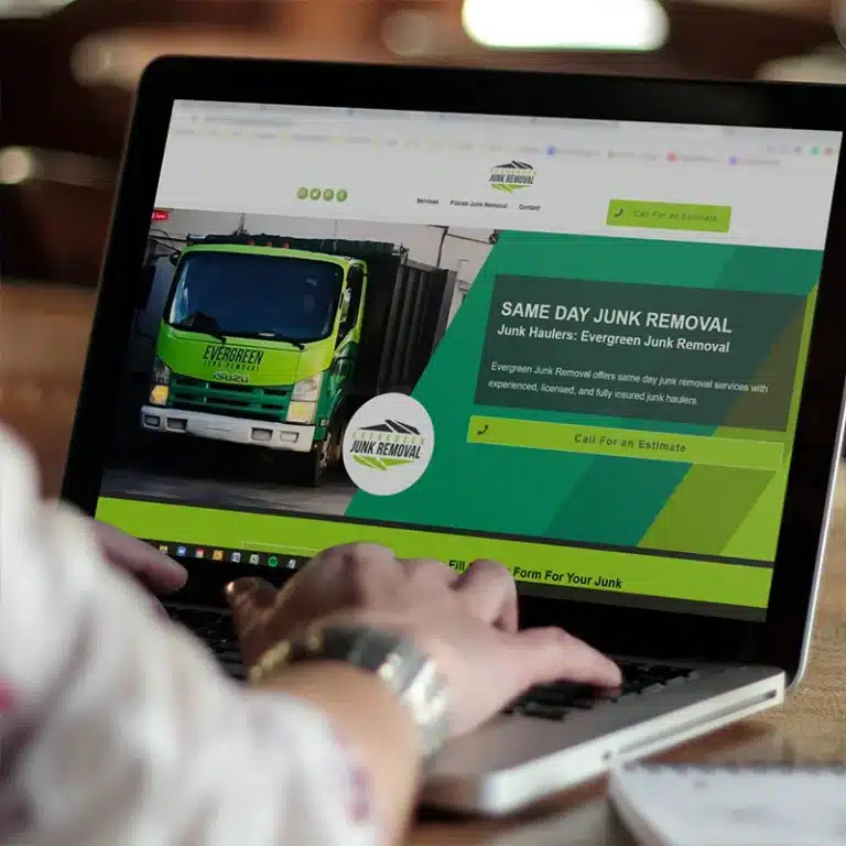 Omaha Branding Company Services Omaha branding services website mockup displayed on a laptop, showing a junk removal company homepage with a bright green service truck, navigation menu, and a call-to-action button, photographed on a wooden table.