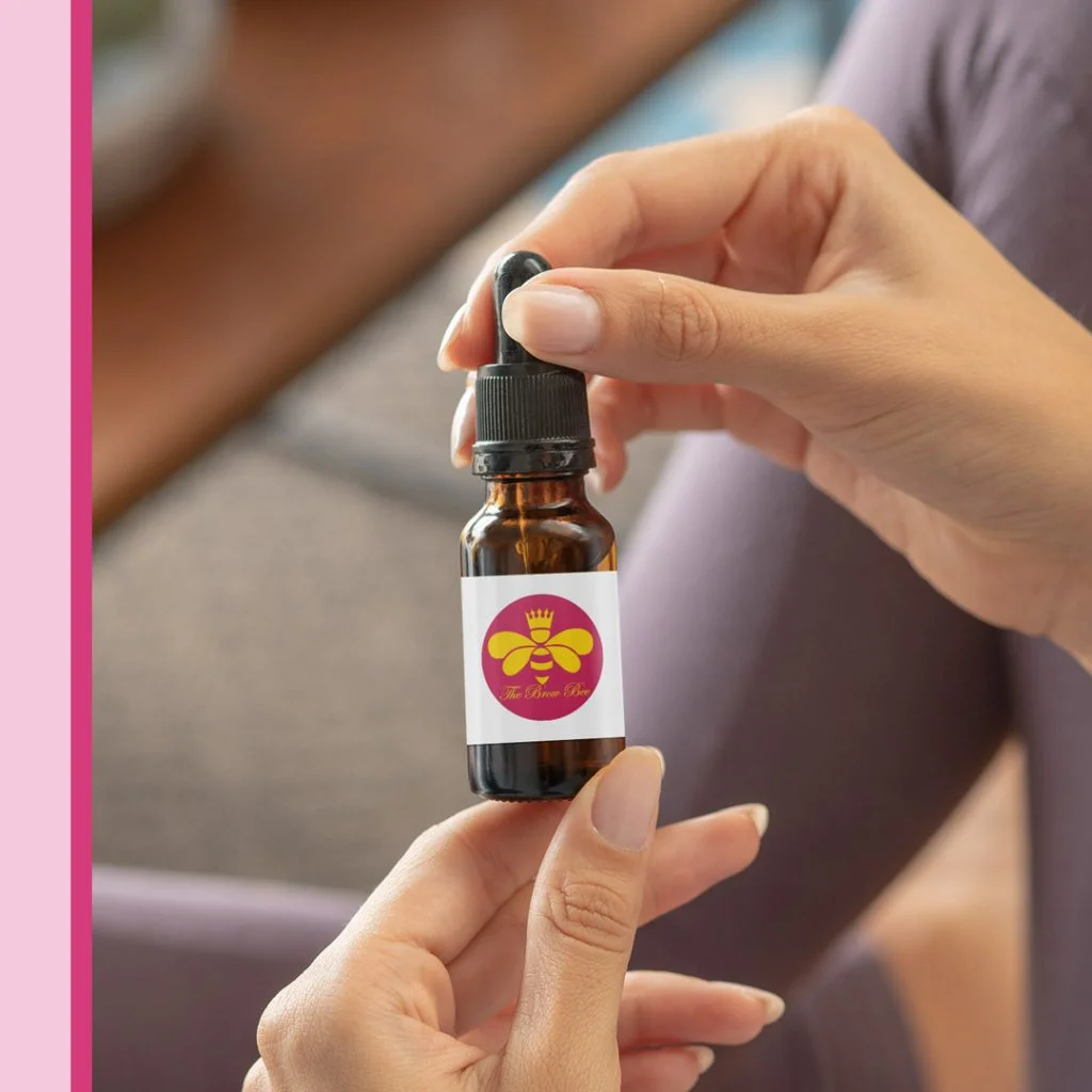 Omaha Branding Services for Beauty Business Omaha branding services product label mockup on an amber glass dropper bottle with a pink and yellow bee logo, held in a person's hands against a lavender-colored top.