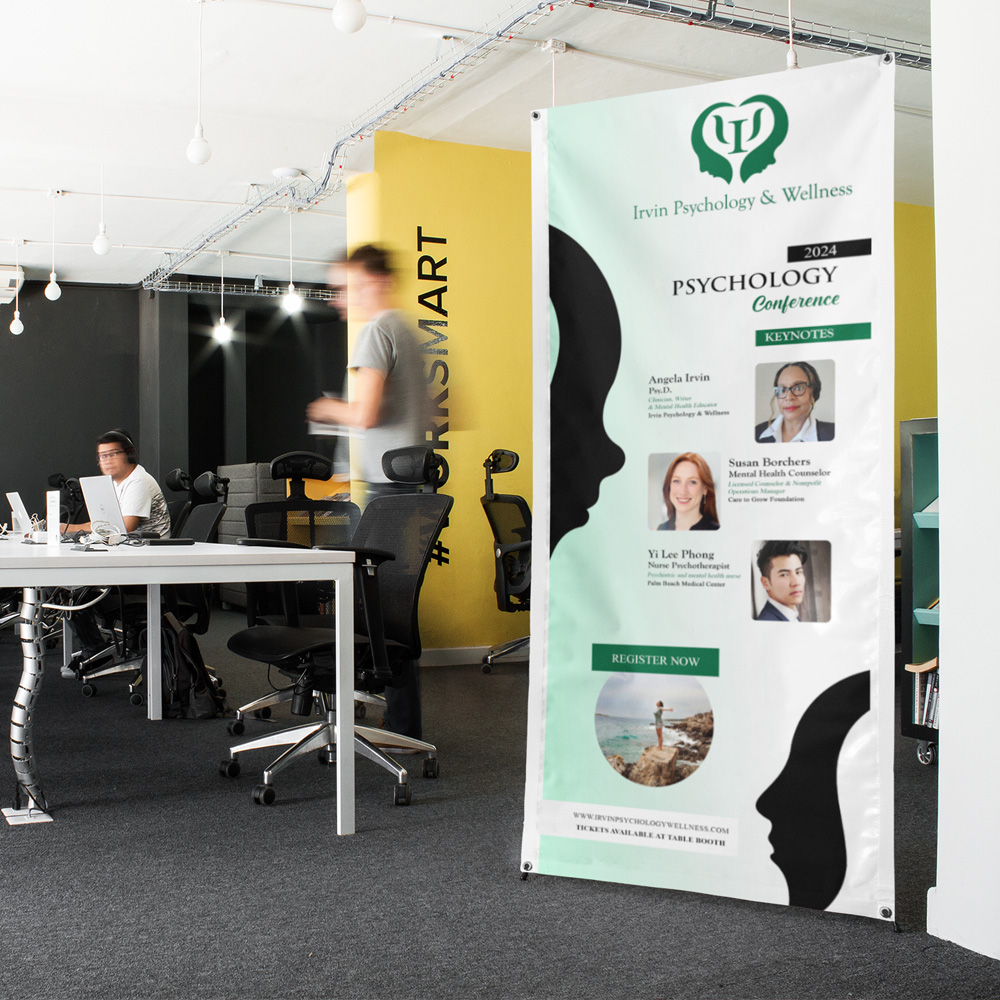 Omaha Logo Designer for Hire A tall vertical vinyl banner hangs in a modern open office with a green heart-shaped emblem at the top, black silhouetted profiles, and headshot portraits down a mint green background, event signage created by an Omaha logo designer.
