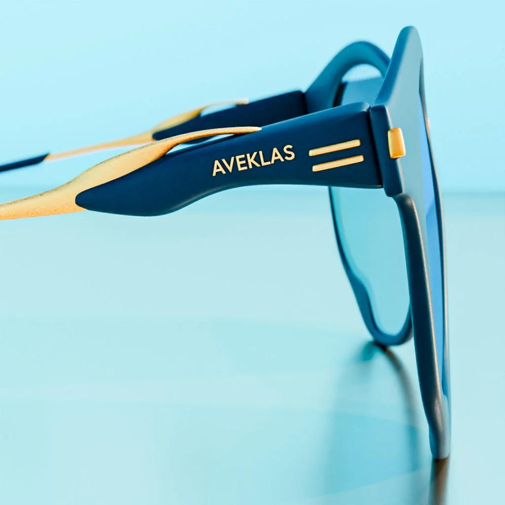 blue-sunglasses-side-profile-view Side view of blue sunglasses with gold arms on a pale blue surface