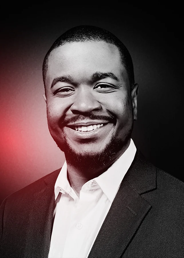 Brand Designer Kenal Louis black and white photograph portrait of brand designer Kenal Louis smiling. With Subtle red gradient to the left side.