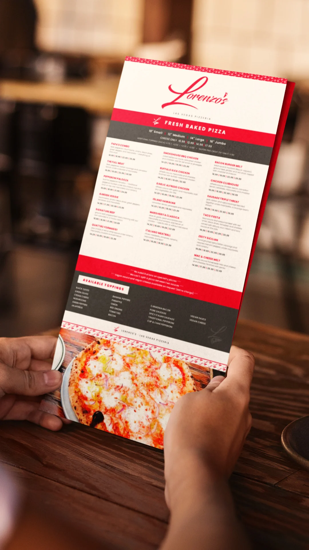 printed-pizza-menu-held-in-hands Person holding a printed Lorenzo's pizza menu at a wooden restaurant table.