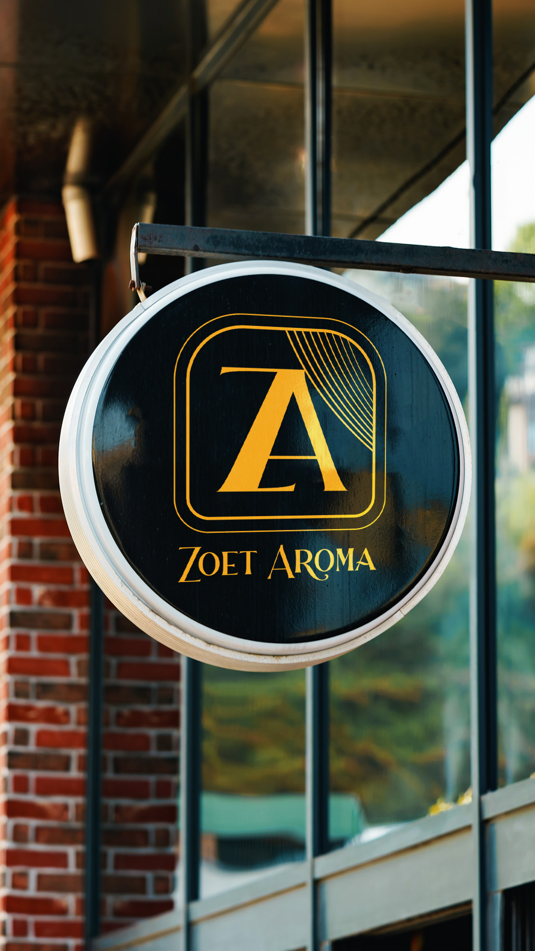 bakery branding design signage Round black hanging sign with a gold Zoet Aroma logo beside a red brick wall.