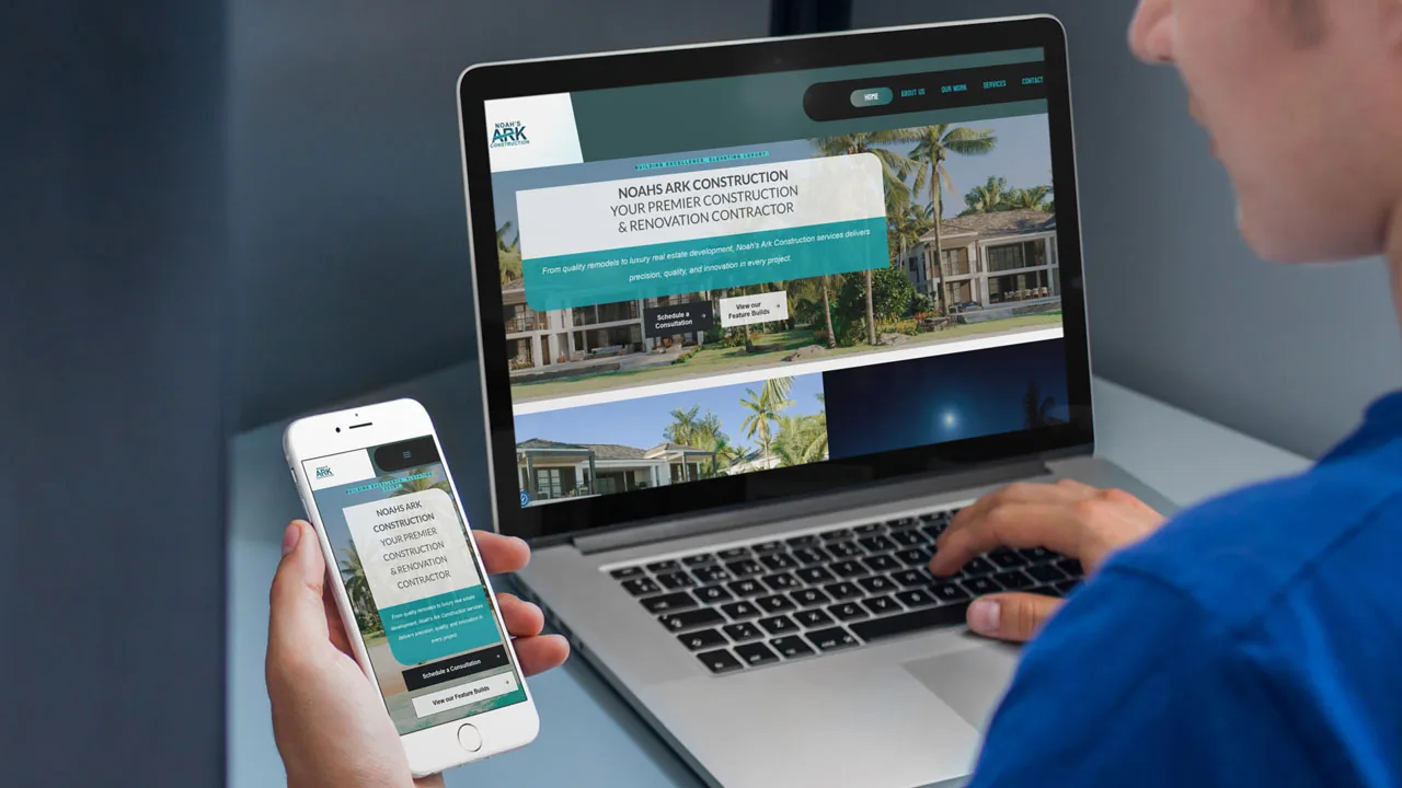 construction-website-design-laptop-phone-mockup Person in a blue shirt holding a phone beside a laptop, both showing a construction website design.