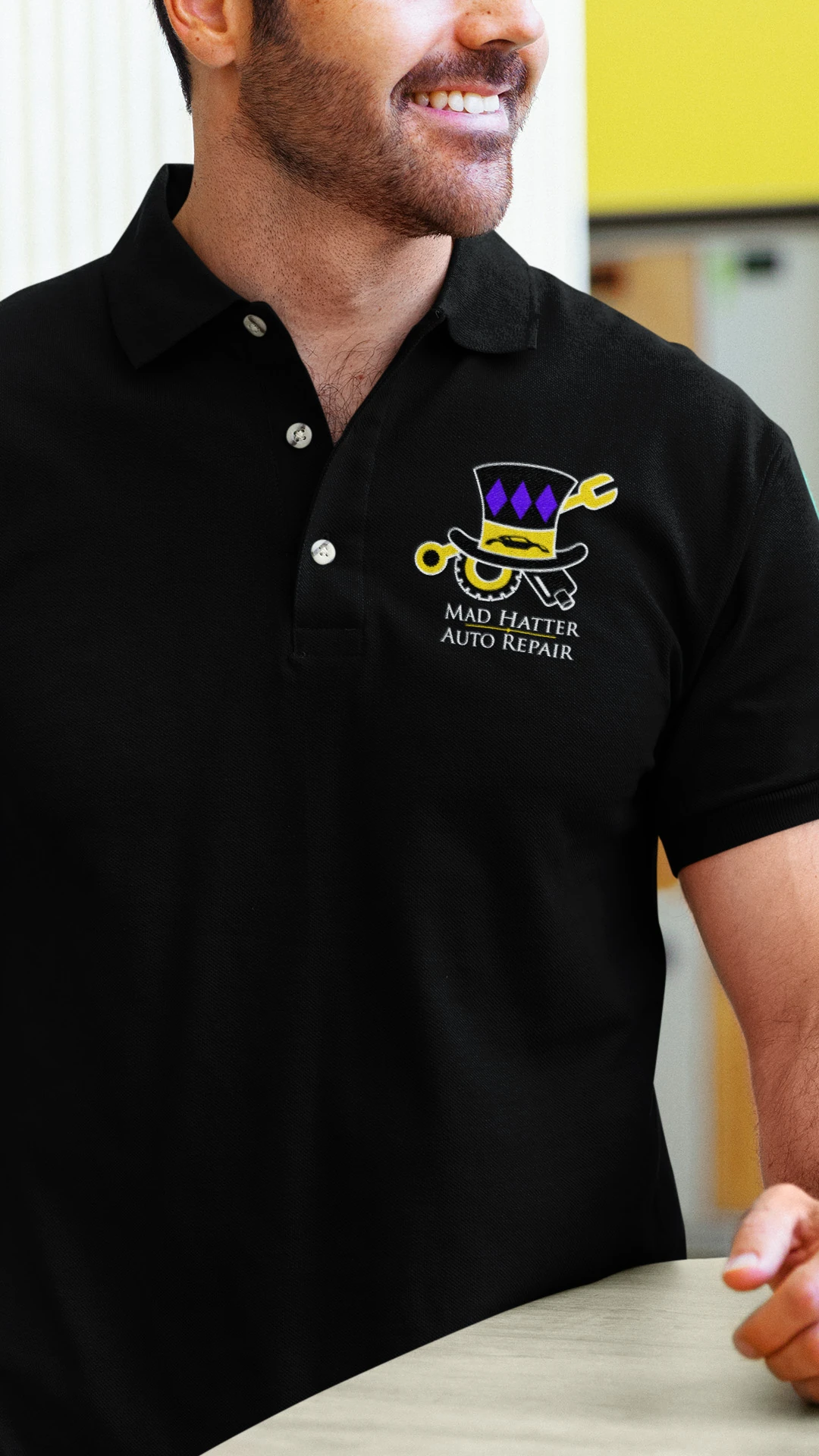 creative-services-mad-hatter-auto-repair-polo-shirt-mockup Man wearing a black polo shirt embroidered with the Mad Hatter Auto Repair logo.