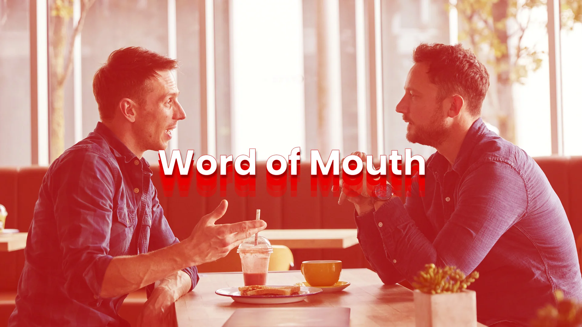 Word of Mouth Conversation at a Cafe Two men in denim shirts talk across a cafe table under a warm red tint, a word-of-mouth moment.