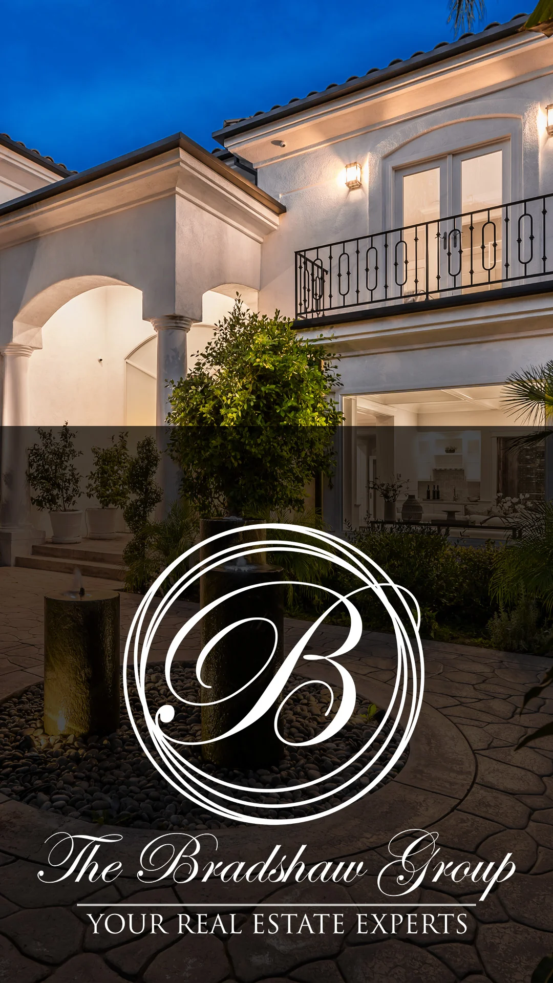 White circular monogram logo overlaid on a dusk view of a luxury home with balcony and courtyard fountains, real estate branding. Real Estate Logo Over Luxury Home Courtyard